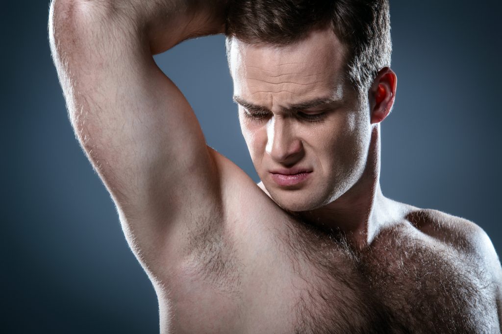 Studio portrait of handsome young man. Clean shaven man with naked torso looking at armpit