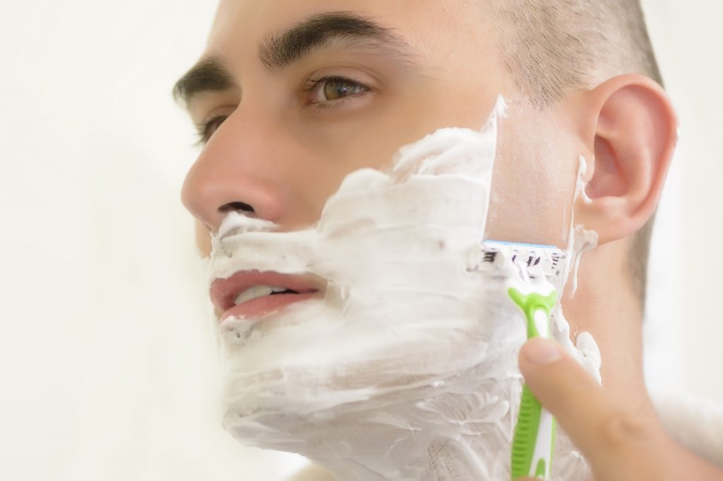 Young man shaving using shaving blade
